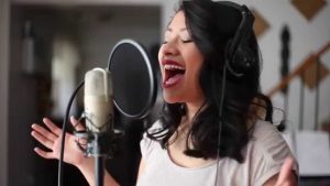 Angela Apigo sings into a recording mic with passion and a smile on her face. 