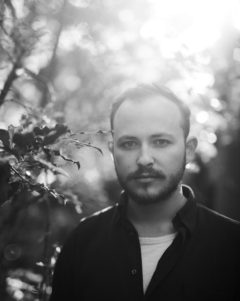 a black and white portrait of Kaine Francesco outdoors in the forest with the sun pouring over his shoulder